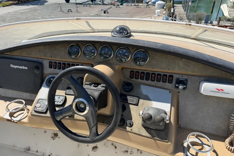 Slide: The Image of 2003 Carver 360 Sport Sedan boat with worn seating on deck, surrounded by greenery. - 10