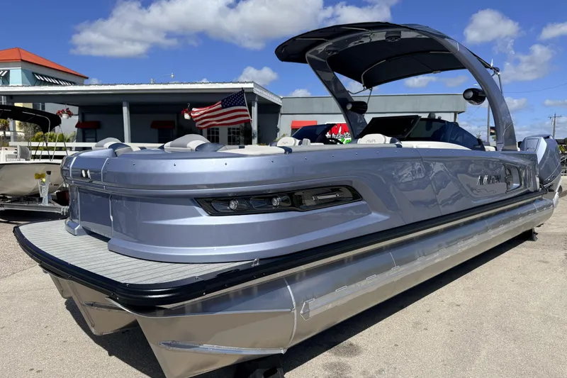 The Image of 2026 Avalon Excalibur Windshield Quad Lounger boat with twin Mercury 425hp engines, docked outdoors. - 0