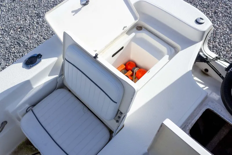 Slide: The Image of 2014 NauticStar 2400 Sport boat seat with storage compartment open, revealing safety gear. - 30