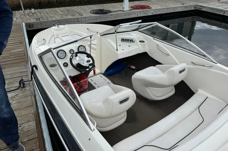 Slide: The Image of 2010 Larson LX 1750 boat interior with white seating and dashboard at a dock. - 7