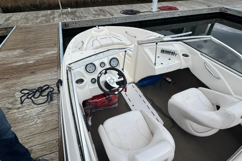 Slide: The Image of 2010 Larson LX 1750 boat interior at dock, featuring steering wheel and white seats. - 9