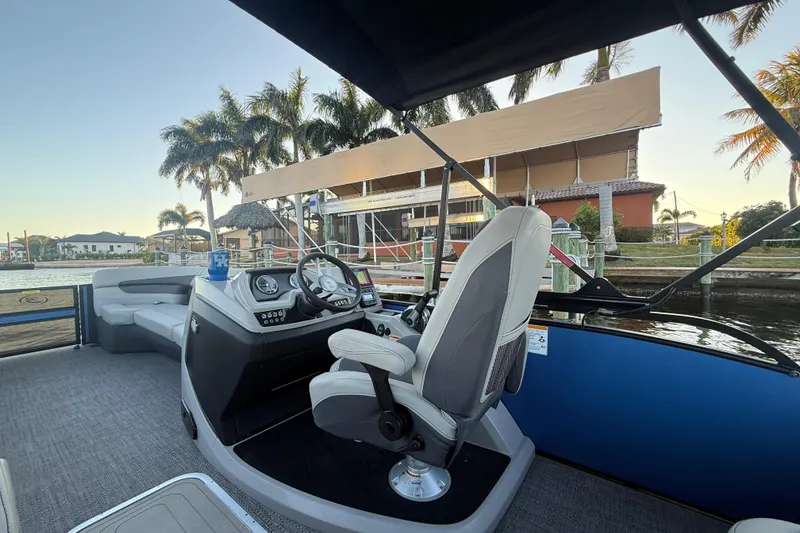 Slide: The Image of 2024 Barletta Cabrio 24UC boat interior with steering wheel, seating, and waterfront view. - 34