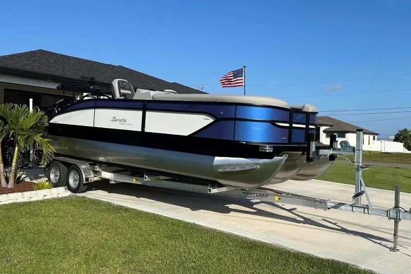 Slide: The Image of 2024 Barletta Cabrio 24UC pontoon boat on trailer, parked in driveway with American flag. - 36