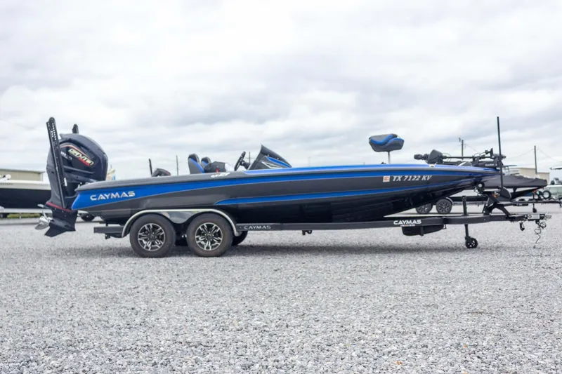 Slide: The Image of 2023 Caymas CX 21 PRO boat on trailer, blue and black design, parked on gravel. - 12