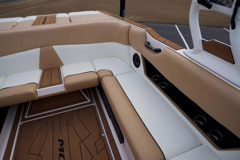 Slide: The Image of 2024 Moomba Max boat interior with tan and white seating, wood accents, and built-in speakers. - 12