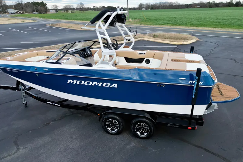 Slide: The Image of 2024 Moomba Max boat in blue and white, parked on a trailer in a lot. - 2