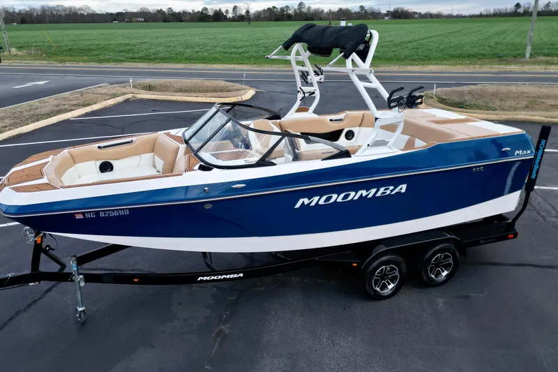 Slide: The Image of 2024 Moomba Max boat in blue and white on a trailer, parked near a green field. - 22