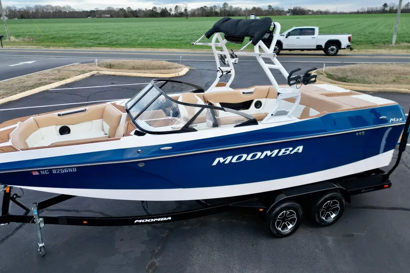 Slide: The Image of 2024 Moomba Max boat in blue and white on a trailer, parked near a green field. - 23