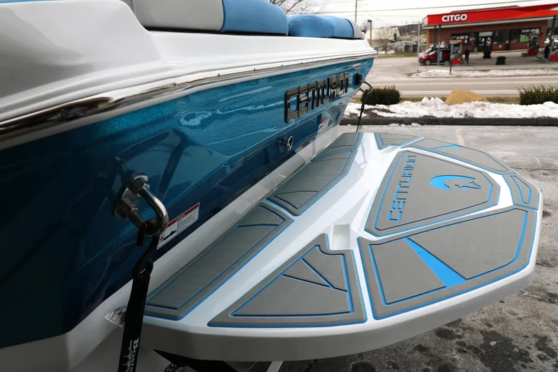 Slide: The Image of 2026 Centurion Nv233 boat with blue and gray detailing, parked near a Citgo station. - 23