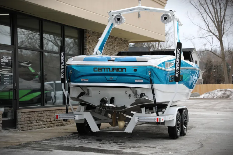 Slide: The Image of 2026 Centurion Nv233 boat on trailer, blue and white design, parked outside dealership. - 4