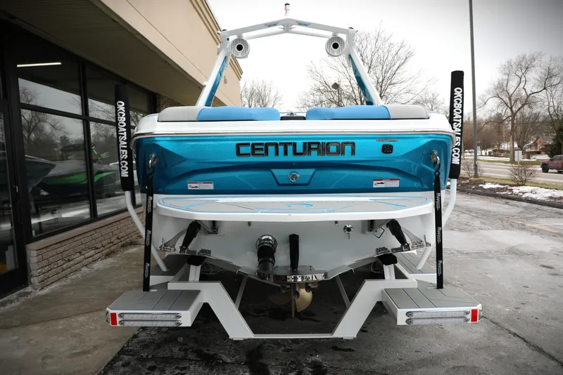 Slide: The Image of 2026 Centurion Nv233 boat, blue and white, rear view in a dealership lot. - 6