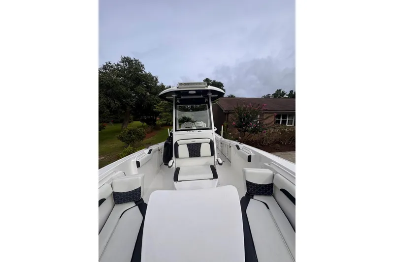 Slide: The Image of 2021 Tidewater 272 CC Adventure boat interior with seating and console, parked near greenery. - 8