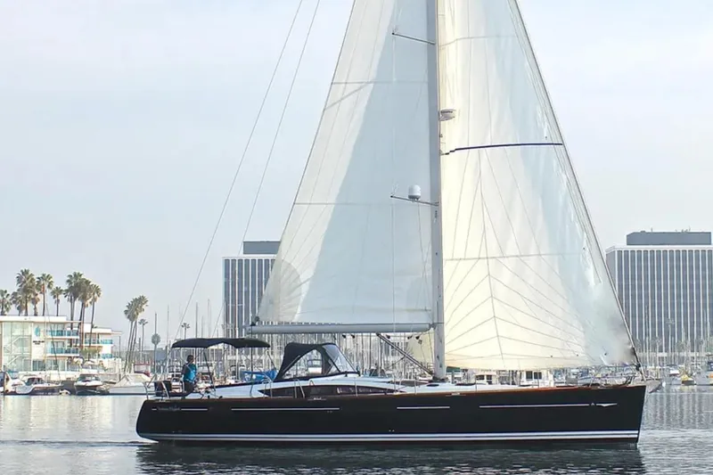 Slide: The Image of 2011 Jeanneau 57 sailboat cruising in a marina with palm trees and buildings. - 2