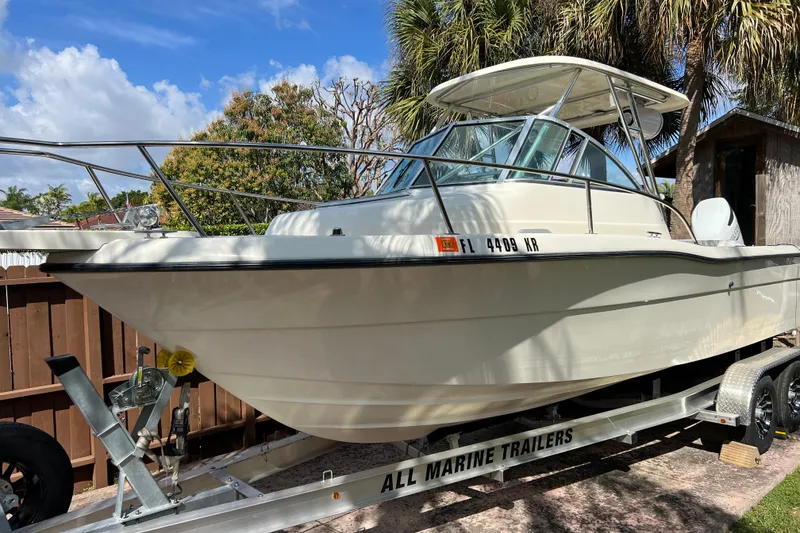 Slide: The Image of 1999 Pursuit 2470 Walkaround boat on trailer, surrounded by palm trees. - 1