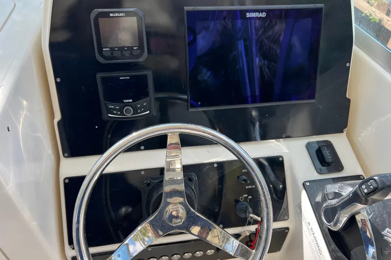 Slide: The Image of 1999 Pursuit 2470 Walkaround boat dashboard with steering wheel, Simrad display, and Suzuki controls. - 19