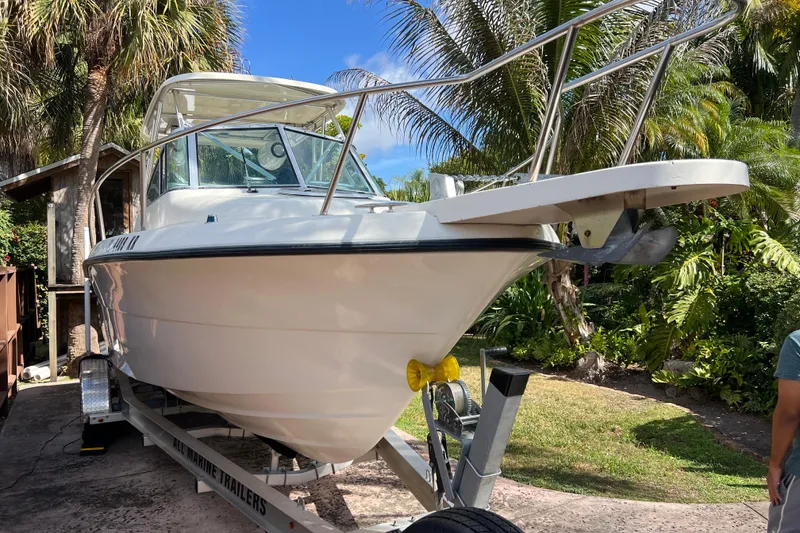 Slide: The Image of 1999 Pursuit 2470 Walkaround boat on trailer, surrounded by tropical foliage. - 2