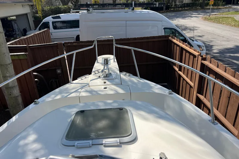 Slide: The Image of 1999 Pursuit 2470 Walkaround boat docked near wooden fence and parked vans. - 22