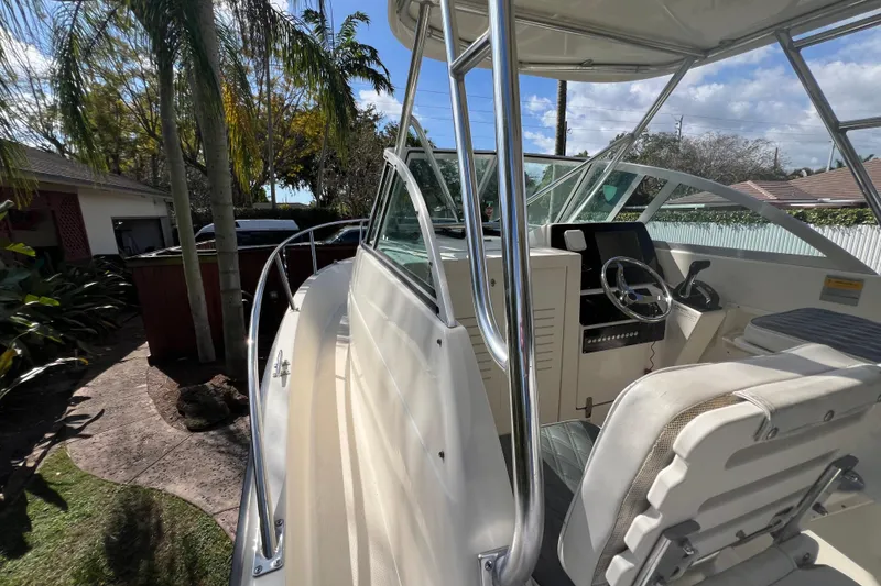 Slide: The Image of 1999 Pursuit 2470 Walkaround boat with helm, palm trees, and sunny sky. - 25