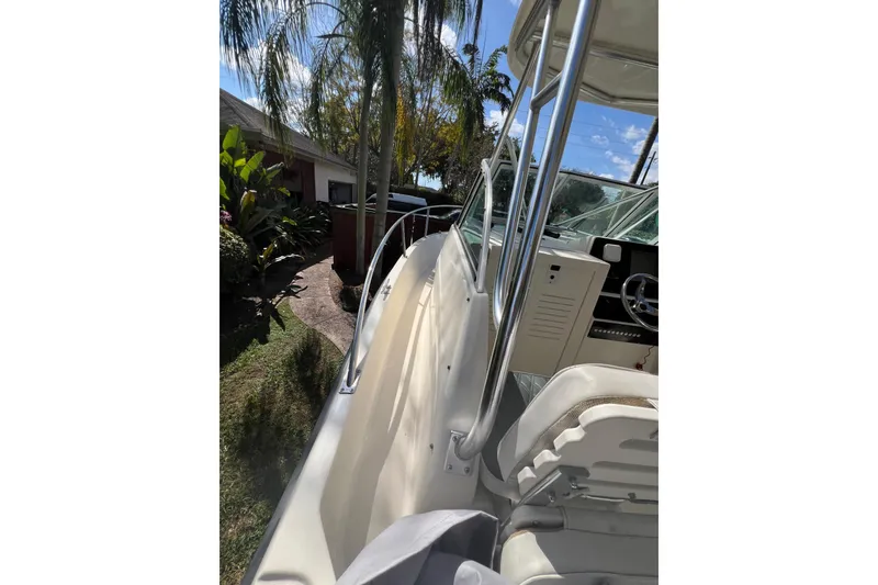 Slide: The Image of 1999 Pursuit 2470 Walkaround boat, side view with cockpit and lush garden background. - 26