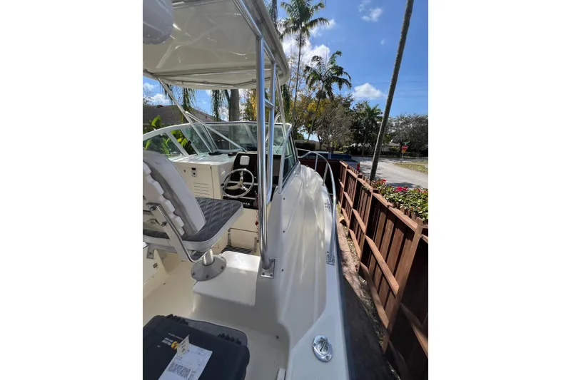 Slide: The Image of 1999 Pursuit 2470 Walkaround boat cockpit with steering wheel and seating, under clear blue sky. - 27