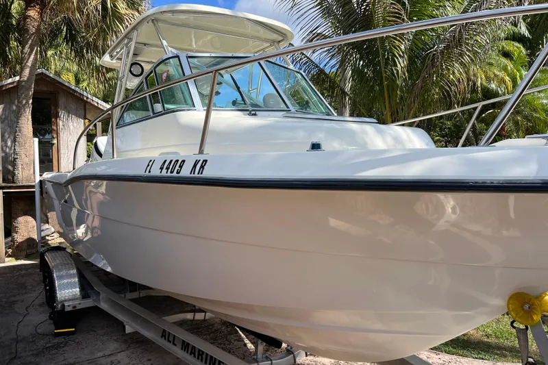 Slide: The Image of 1999 Pursuit 2470 Walkaround boat on trailer, surrounded by palm trees. - 4