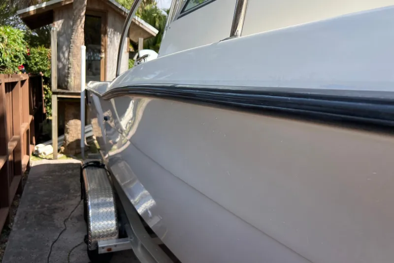 Slide: The Image of 1999 Pursuit 2470 Walkaround boat on trailer beside wooden fence and small shed. - 6