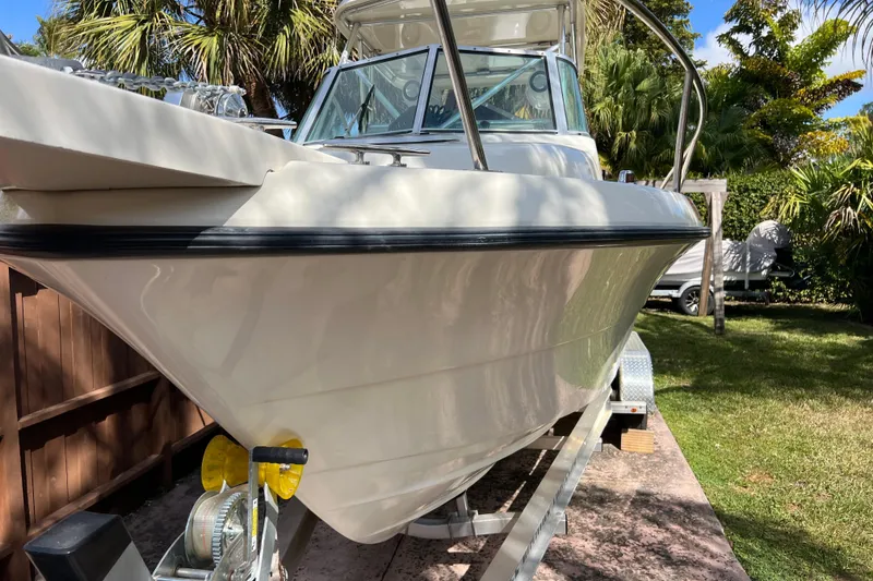 Slide: The Image of 1999 Pursuit 2470 Walkaround boat on trailer, surrounded by lush greenery. - 9