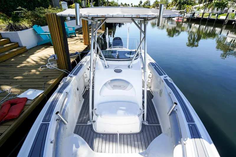 Slide: The Image of 2004 Boston Whaler 240 Outrage docked by a serene waterfront with lush greenery. - 24