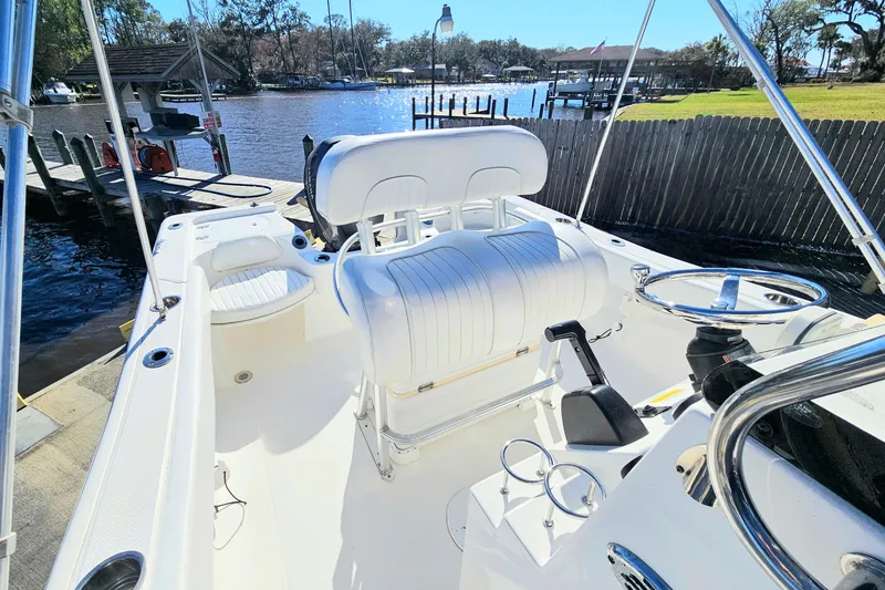 Slide: The Image of 2014 Sea Fox 199 Commander boat interior with white seating and steering wheel, docked by a scenic waterfront. - 11