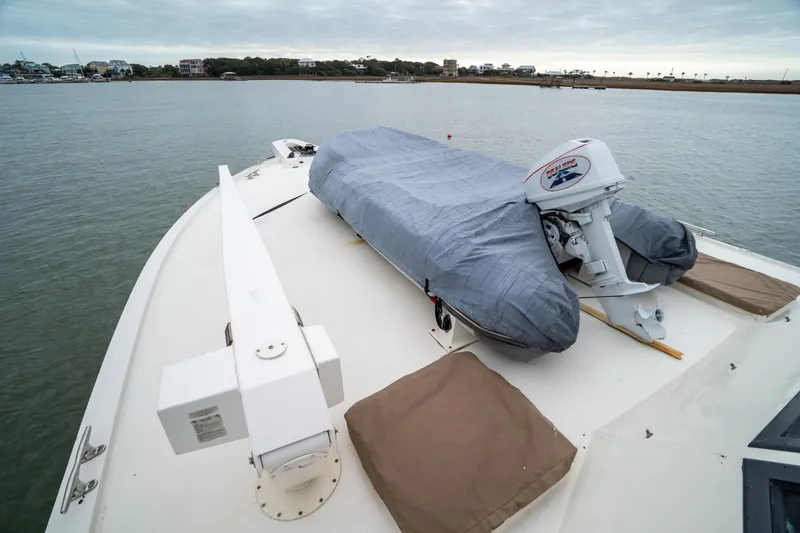 Slide: The Image of 1984 Hatteras 52 Convertible yacht with covered dinghy on deck, moored near shoreline. - 19