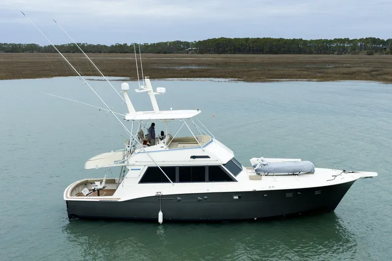 Slide: The Image of 1984 Hatteras 52 Convertible yacht on calm water, featuring a sleek design and fishing equipment. - 6