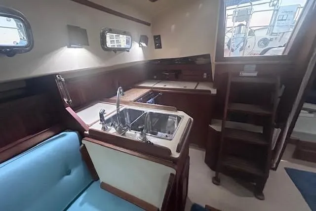 Slide: The Image of Interior of 1994 Island Packet 320 sailboat, featuring a compact kitchen and seating area. - 13