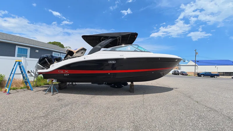 Slide: The Image of The image shows a Sea Ray SLX 280 Outboard boat in a parking lot. It features a black and white design with a red stripe. - 31