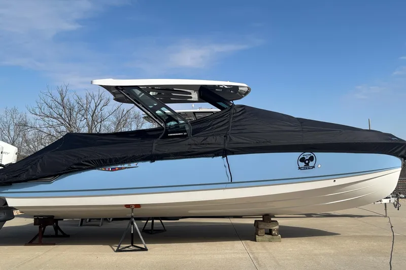 The Image of 2026 Monterey Elite 30 OB boat covered, parked on a concrete surface under a clear sky. - 1