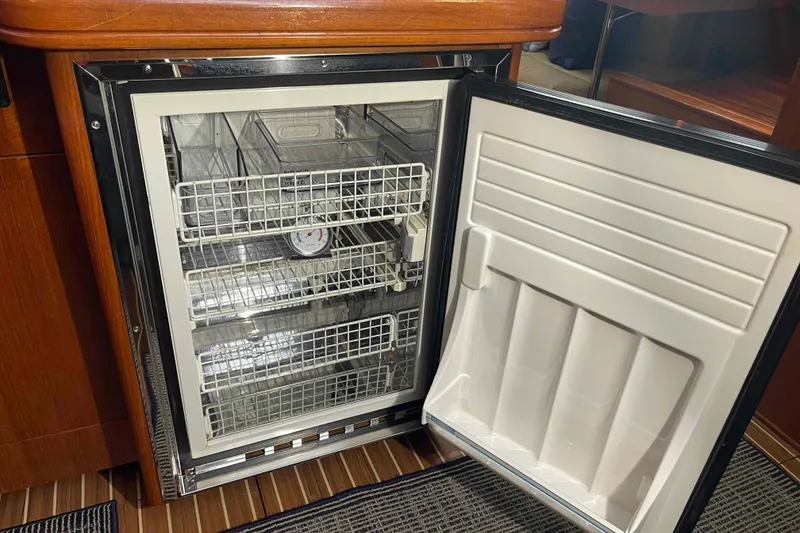 Slide: The Image of Open refrigerator inside 2003 Hunter 426 Deck Salon yacht, featuring wire shelves and wooden cabinetry. - 28