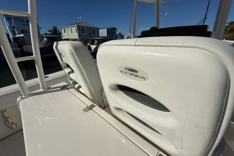 Slide: The Image of 2022 Cobia 320 Center Console boat seats with logo, docked near waterfront homes. - 19