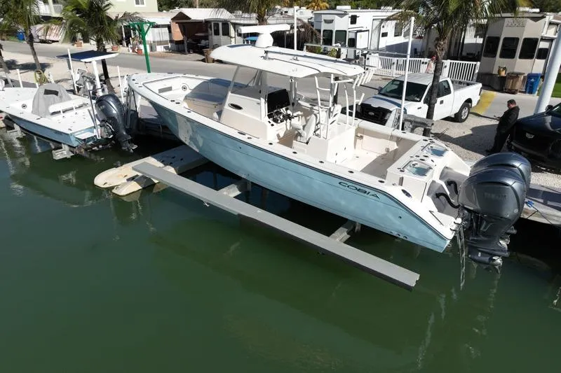 Slide: The Image of 2022 Cobia 320 Center Console boat docked at marina with dual engines. - 2