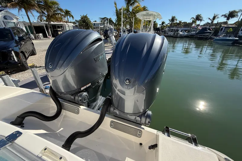 Slide: The Image of 2022 Cobia 320 Center Console with twin Yamaha outboard motors docked by palm trees. - 30