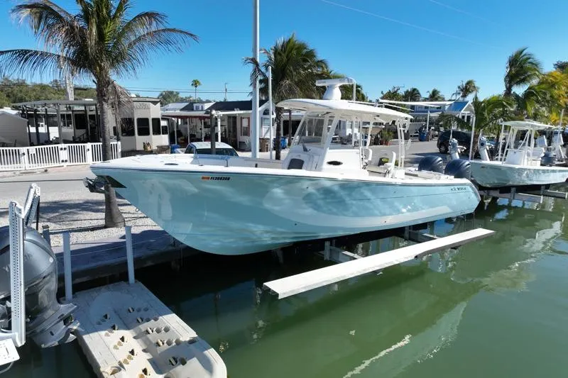 Slide: The Image of 2022 Cobia 320 Center Console boat docked by palm trees and waterfront homes. - 4