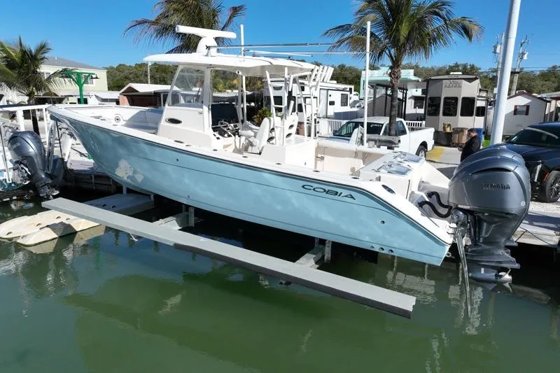 Slide: The Image of 2022 Cobia 320 Center Console boat docked with dual engines, surrounded by palm trees. - 5
