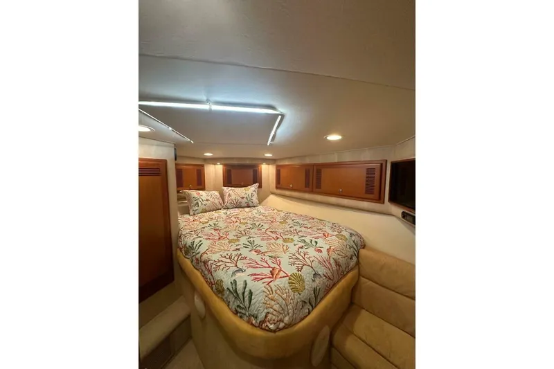 Slide: The Image of 2004 Cabo 48 Flybridge cabin with floral bedding and wooden storage cabinets. - 32