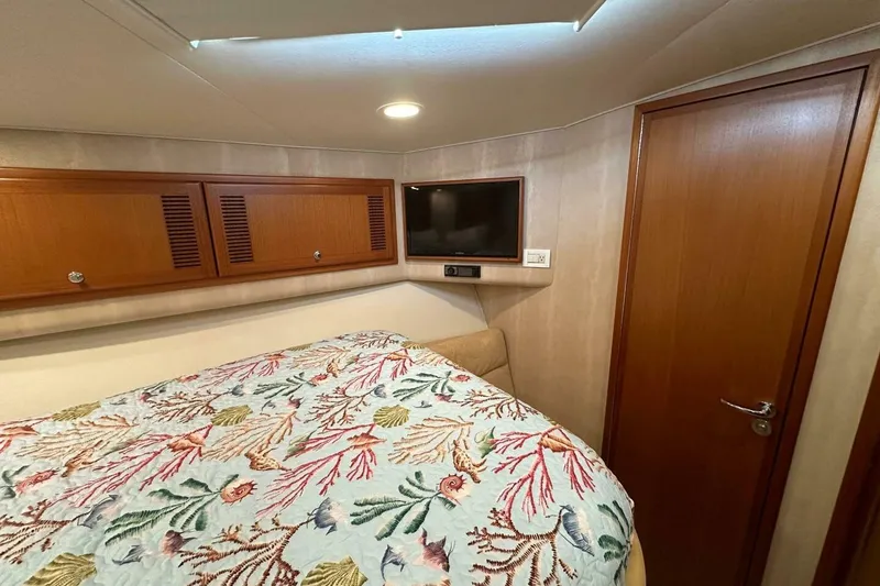 Slide: The Image of 2004 Cabo 48 Flybridge cabin with floral bedding, wooden cabinets, and a wall-mounted TV. - 33
