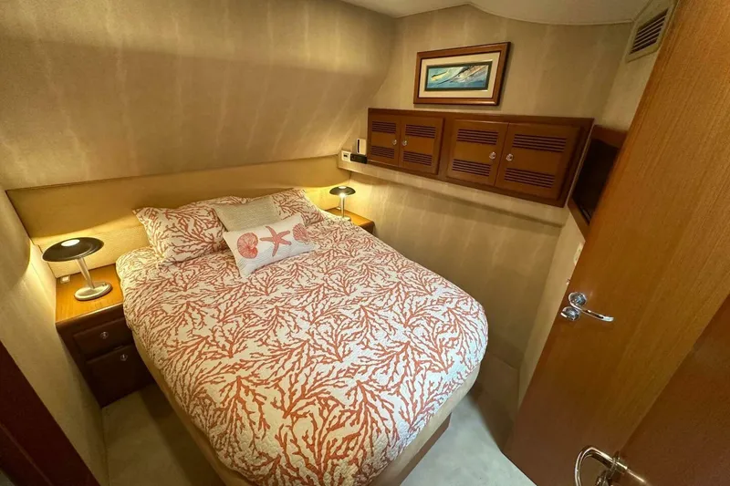 Slide: The Image of 2004 Cabo 48 Flybridge cabin with coral-patterned bedding and wooden storage cabinets. - 34