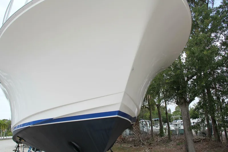Slide: The Image of 2004 Cabo 48 Flybridge boat hull, white and blue, on land with trees in background. - 54