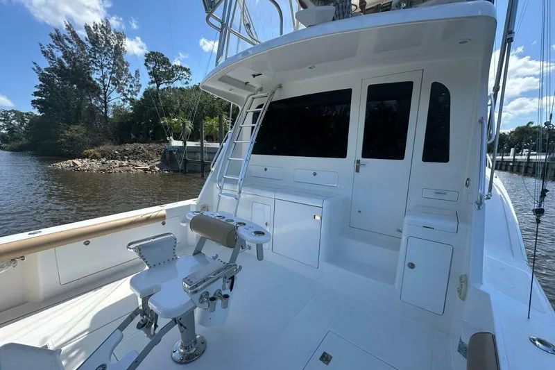 Slide: The Image of 2004 Cabo 48 Flybridge yacht with fishing chair, docked by a scenic riverbank. - 56