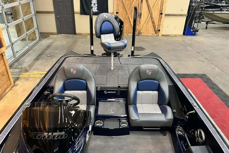 Slide: The Image of 2023 Triton 20 TrX Patriot boat interior with blue and gray seating in a showroom. - 14