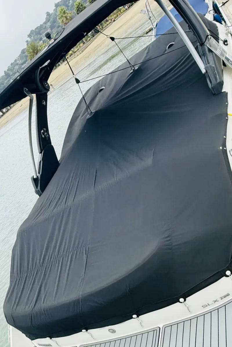 Slide: The Image of 2020 Sea Ray SLX 280 boat with black cover, docked near a sandy beach. - 26