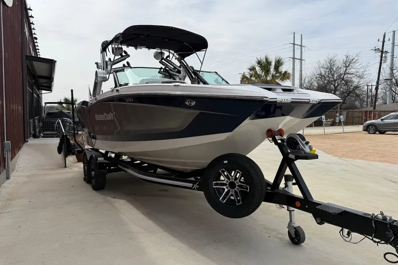Slide: The Image of 2024 MasterCraft X24 boat on trailer, parked outdoors near a building. - 2