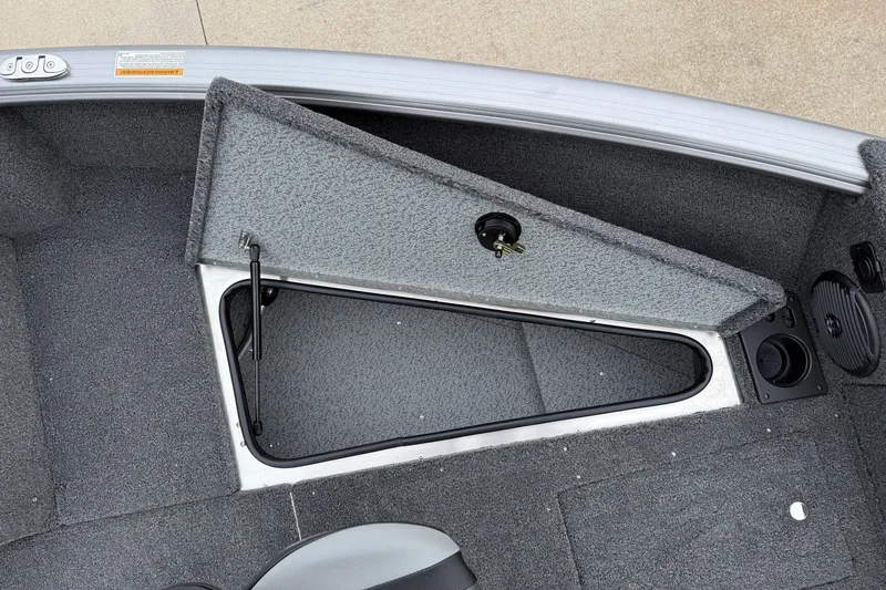 Slide: The Image of 2026 Lund 1875 Impact XS Sport boat storage compartment with open hatch and carpeted interior. - 12