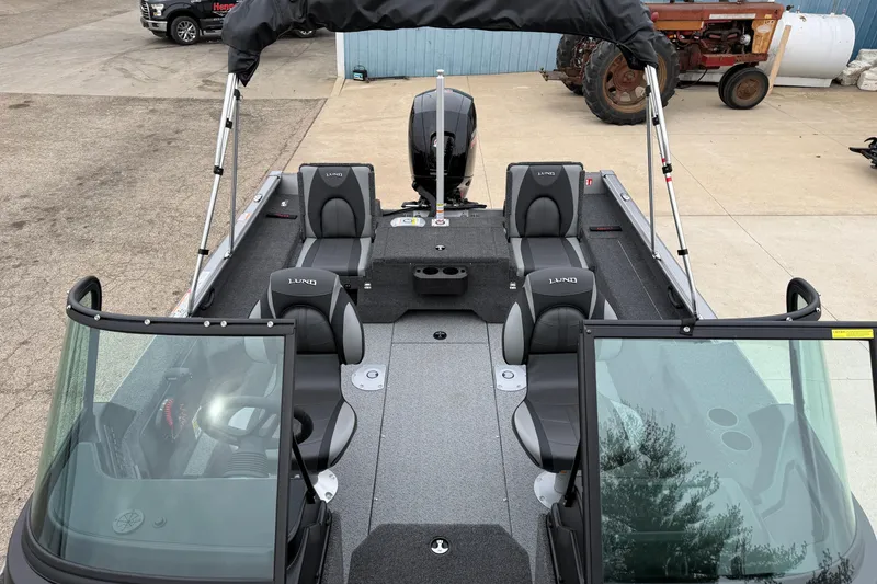Slide: The Image of 2026 Lund 1875 Impact XS Sport boat interior with seating and canopy, parked outdoors. - 15